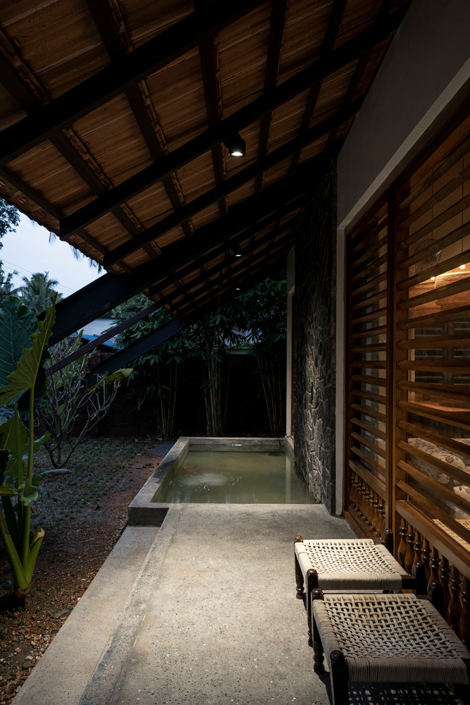 Cửa có mái che bằng gỗ theo phong cách truyền thống ở mặt tiền, sàn bê tông kết hợp khảm đá trên tường trong khi đồ nội thất được thiết kế theo phong cách xưa cũ.