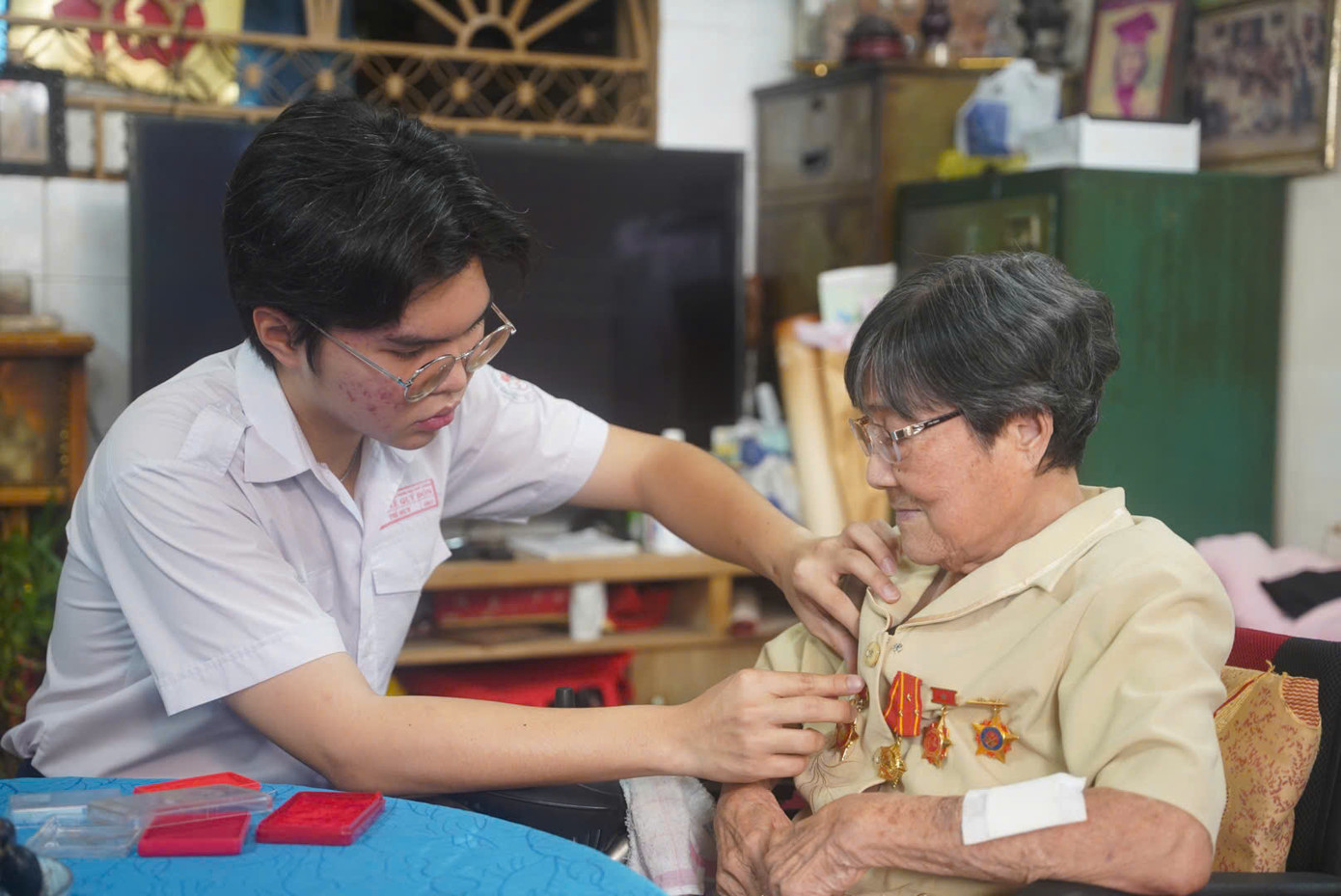 Người cháu trai út gắn huy chương lên áo bà Trần Bội Trang. Hơn nửa thế kỷ trôi qua, bà nói điều khiến mình hạnh phúc nhất là được thấy đất nước hôm nay thanh bình, tươi đẹp và phát triển. Ảnh: Phú Quang