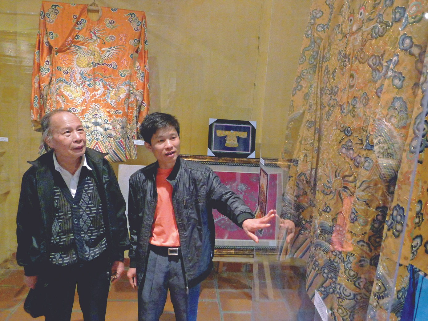 Nghệ nhân Vũ Văn Giỏi (phải) đang giới thiệu long bào Vua Đồng Khánh với khách tham quan. Ảnh: Xuân Phú