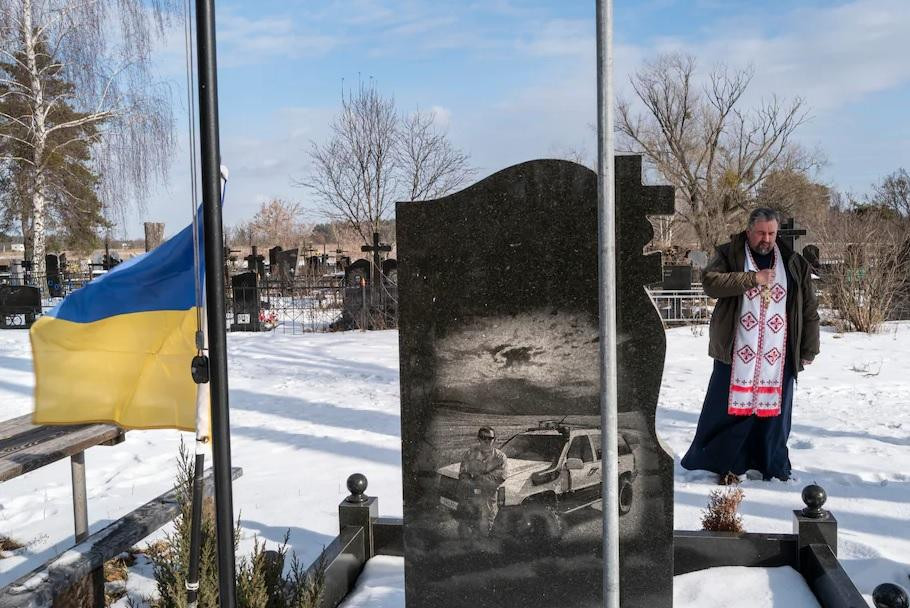 Linh mục Kostyantyn Kholodov, một tuyên úy quân đội, cầu nguyện ngày 6/22 ở Bucha, Ukraine, bên ngôi mộ của hai người đàn ông địa phương thiệt mạng trong cuộc xung đột với lực lượng ly khai ở miền đông nước này. Ảnh: The Washington Post.