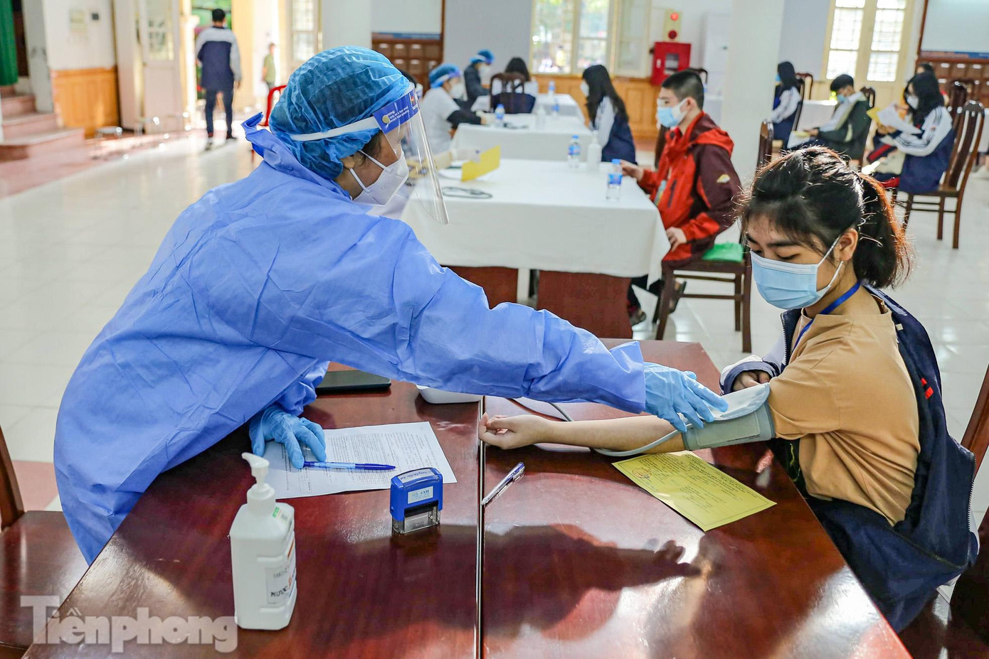 Sau khi đến lượt được gọi tên, học sinh được khám sàng lọc, đo huyết áp trước khi vào tiêm vắc xin phòng COVID-19.