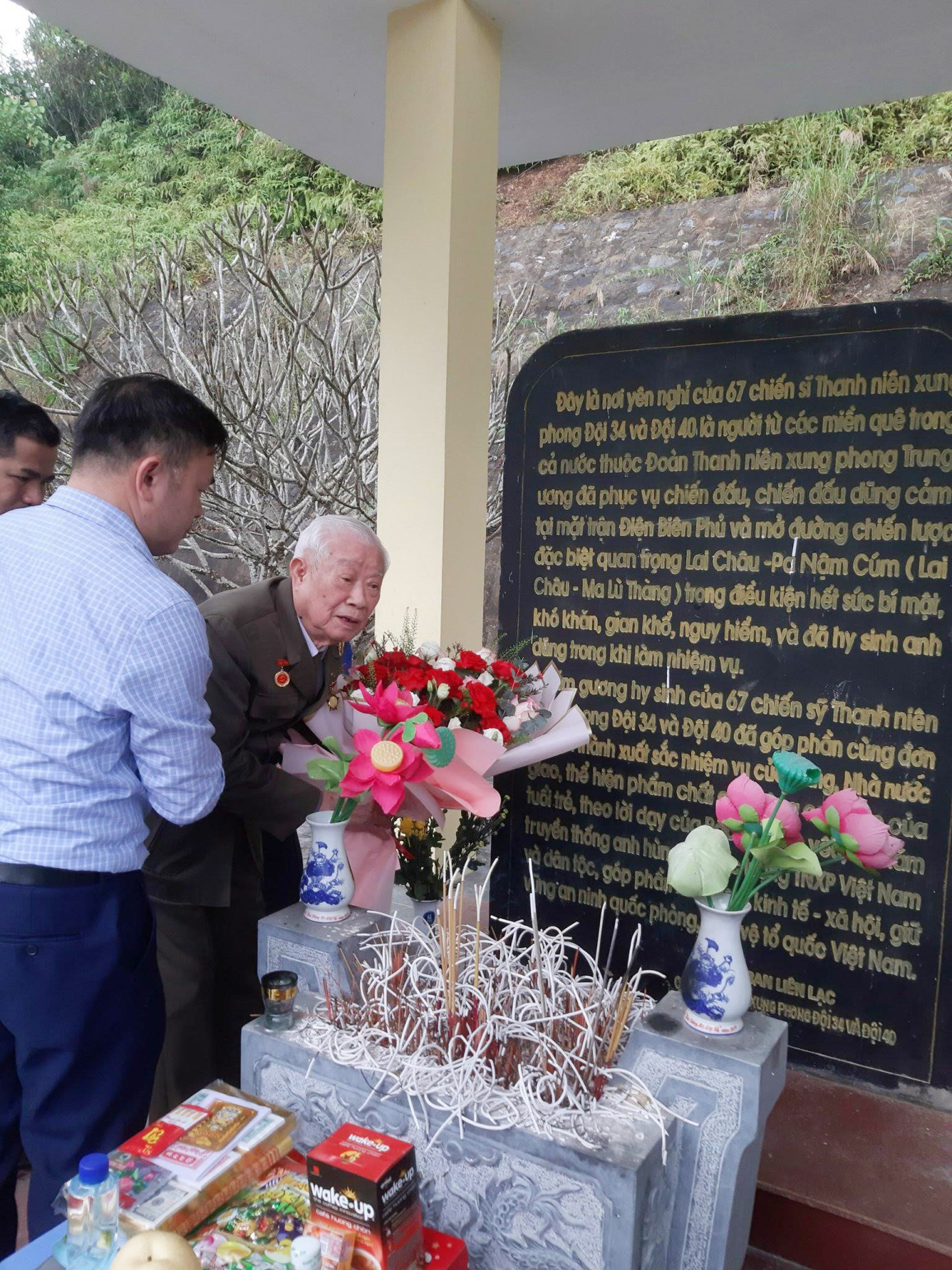 Cựu TNXP Nguyễn Tiến Năng bên tấm bia ghi dấu nơi yên nghỉ của 67 TNXP đã tham gia xây dựng tuyến đường Ma Lù Thàng – thị xã Lai Châu. Ảnh: NHÂN VẬT CUNG CẤP