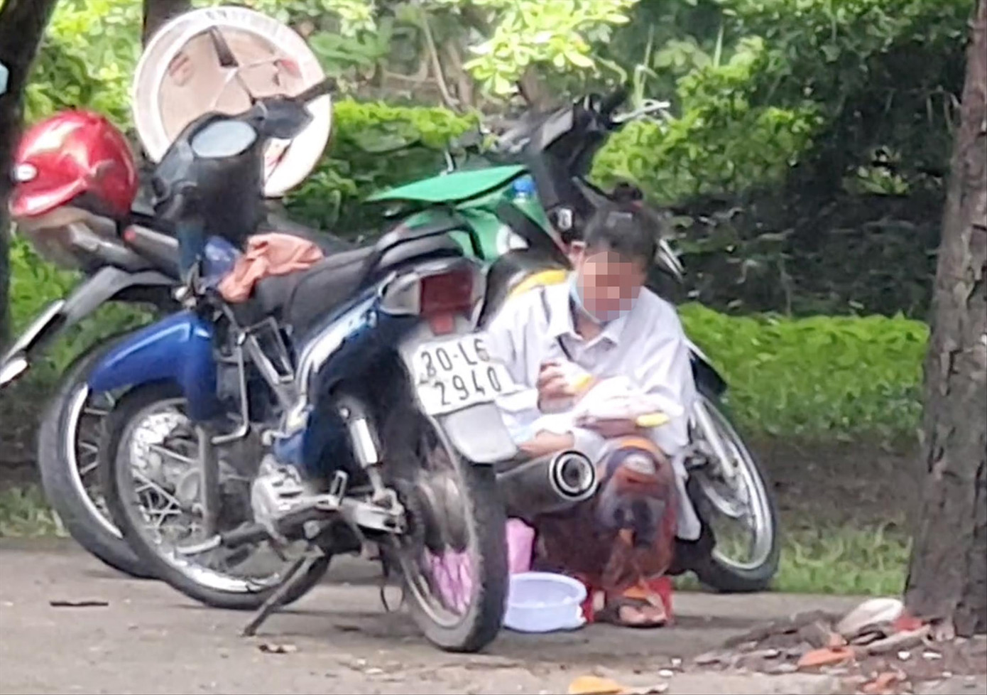 Người phụ nữ ngồi núp sau xe máy để cho bé trai bú sữa bình. Ảnh: Thuận Nhàn. Người phụ nữ ngồi núp sau xe máy để cho bé trai bú sữa bình. Ảnh: Thuận Nhàn.