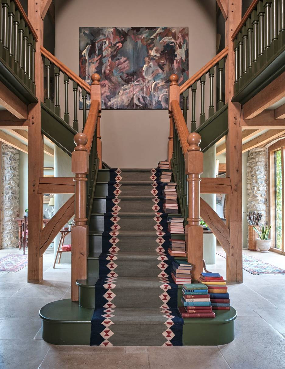 Để giảm bớt sự nặng nề của cầu thang giữa ngôi nhà, cầu thang và lan can được sơn bằng màu “Olive Colour”, kết hợp cùng thảm cầu thang viền hoạ tiết hình học và một bức tranh trừu tượng.