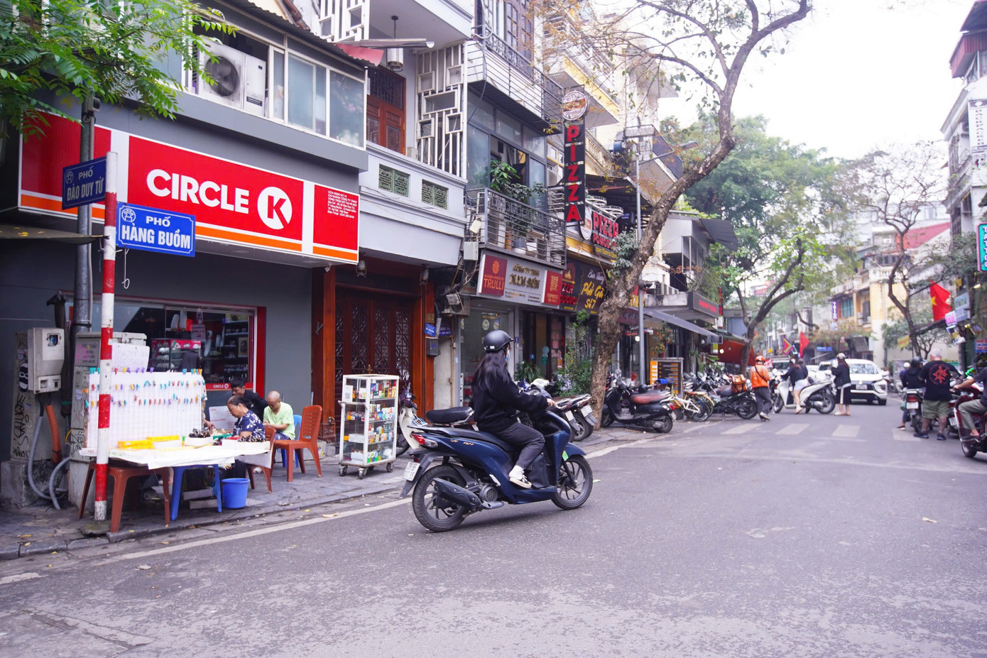Trong ảnh là phố Hàng Đào, trụ sở UBND phường Hàng Đào - gắn liền nguồn gốc từ mặt hàng vải nhuộm đỏ được bán nhiều ở phố. Giao với phố Hàng Đào có phố Hàng Buồm - và cũng có tên phường Hàng Buồm - gắn với lịch sử trước đây là khu vực chuyên bán các loại buồm cho thuyền bè.
