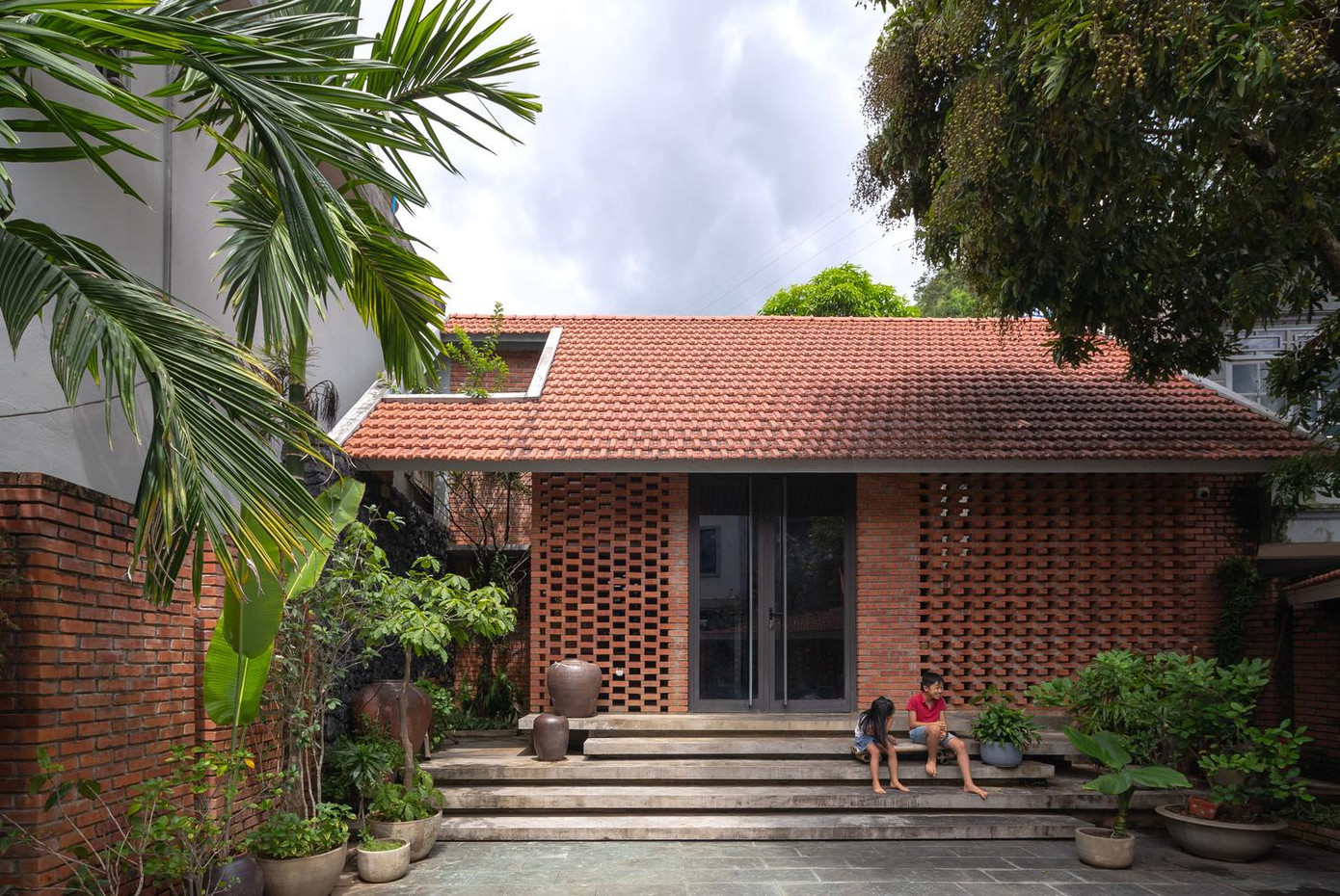 Mảnh đất xây dựng ngôi nhà khá rộng rãi với nhiều cây cổ thụ, nằm trên một sườn đồi thoải có những mỏm đá nhỏ lô nhô, do đó thay vì đổ xi măng, sân trước được lát đá để tạo cảm giác xưa cũ cho không gian.