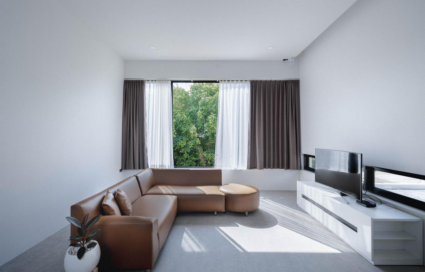 Ở cạnh đầu tiên của chữ U là không gian phòng khách và phòng bếp. Phòng khách được bày trí rất đơn giản với một bộ sofa màu nâu và kệ ti vi. Điểm đặc biệt của phòng khách là có cửa sổ bằng kính lớn để ánh sáng tràn vào nhà và hệ thống ô thoáng sát chân tường để người ngồi trong nhà có thể quan sát được người ở phía ngoài sân.