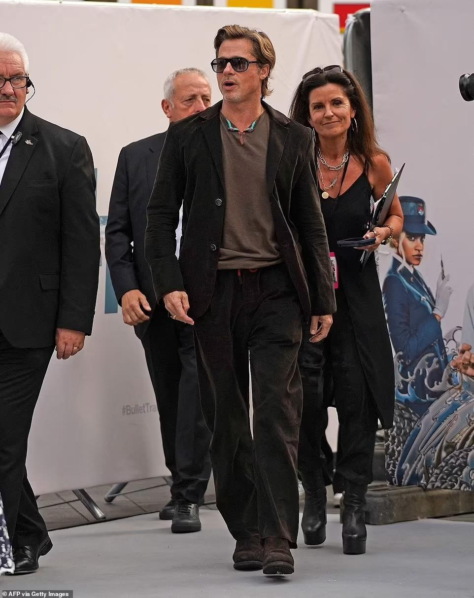 Brad Pitt phong độ ở tuổi 59 khi mặc áo blazer nhung nâu với quần và giày đồng bộ kết hợp áo thun nâu nhạt và kính đen.