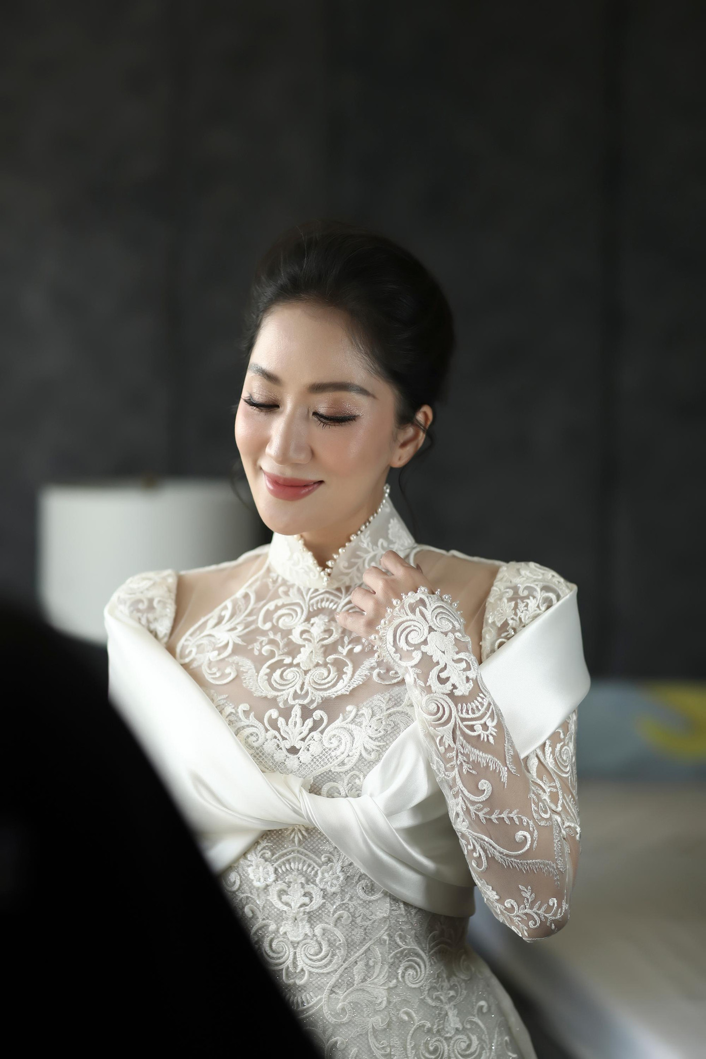 Sáng 12/12, lễ ăn hỏi của Khánh Thi và Phan Hiển được diễn ra tại nhà riêng của hai người. Cô dâu Khánh Thi chọn áo dài ren trắng cách điệu lạ mắt, khoe nhan sắc mặn mà. Chiếc áo dài của Khánh Thi là thiết kế cách tân được làm bằng chất liệu ren Pháp thêu nổi, kết hợp với họa tiết cổ điển hoàng gia và phần choàng bằng chất liệu Italian Mikado uốn lượn, xoắn vào nhau như một dải nơ.