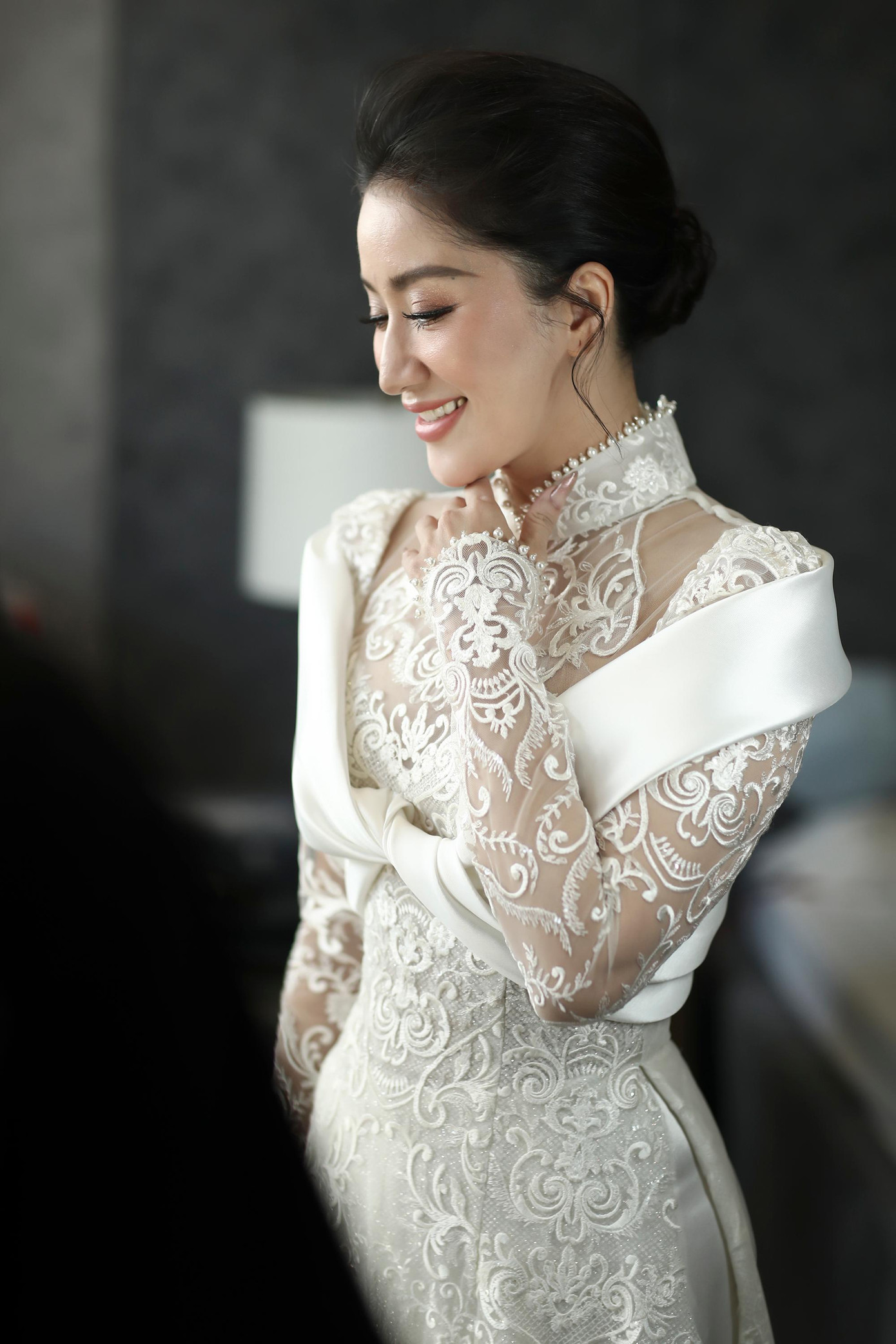 Sáng 12/12, lễ ăn hỏi của Khánh Thi và Phan Hiển được diễn ra tại nhà riêng của hai người. Cô dâu Khánh Thi chọn áo dài ren trắng cách điệu lạ mắt, khoe nhan sắc mặn mà. Chiếc áo dài của Khánh Thi là thiết kế cách tân được làm bằng chất liệu ren Pháp thêu nổi, kết hợp với họa tiết cổ điển hoàng gia và phần choàng bằng chất liệu Italian Mikado uốn lượn, xoắn vào nhau như một dải nơ.