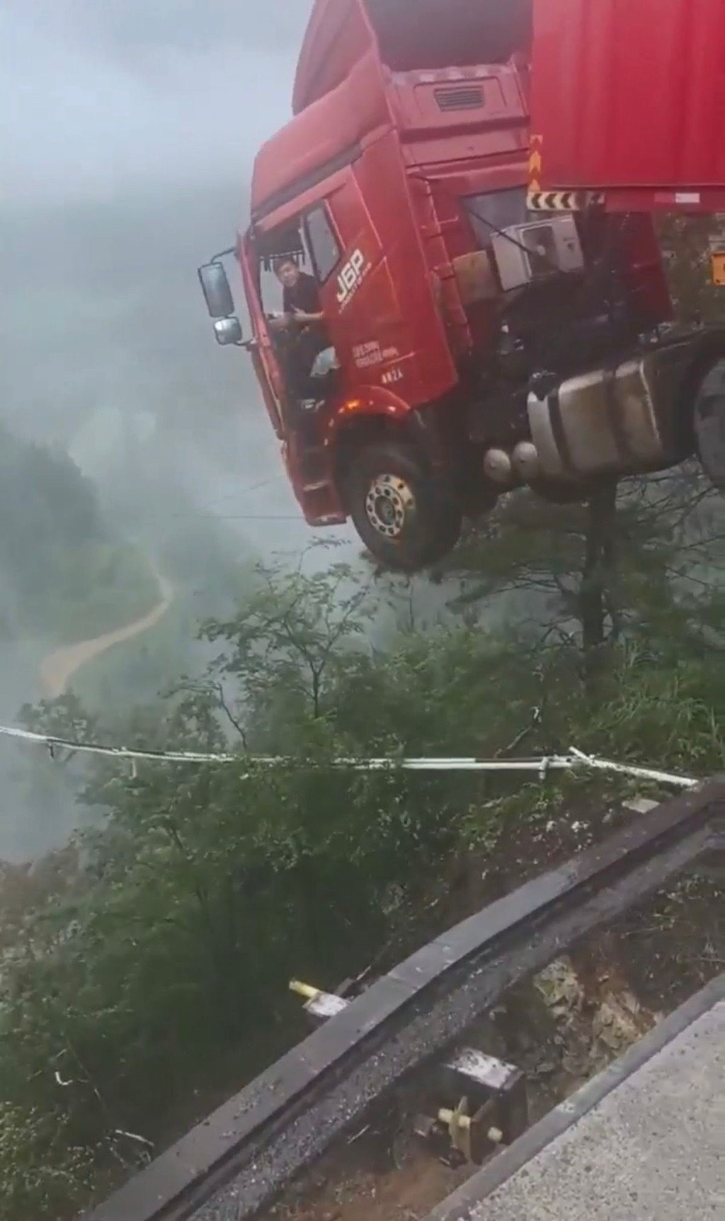 Tài xế mắc kẹt trong cabin xe container nằm cheo leo trên miệng vực sâu 100m. (Ảnh: The Standard)