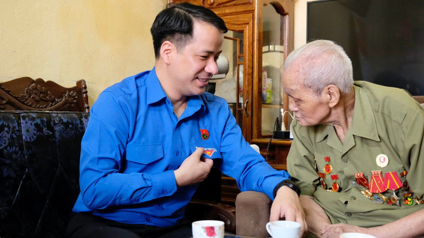 Dù mắt đã kém, ông Hoàng Đình Huệ vẫn chú tâm để đọc được chữ "Thanh niên Việt Nam" trên áo của anh Ngô Văn Cương. Ảnh: Châu Linh Dù mắt đã kém, ông Hoàng Đình Huệ vẫn chú tâm để đọc được chữ "Thanh niên Việt Nam" trên áo của anh Ngô Văn Cương. Ảnh: Châu Linh