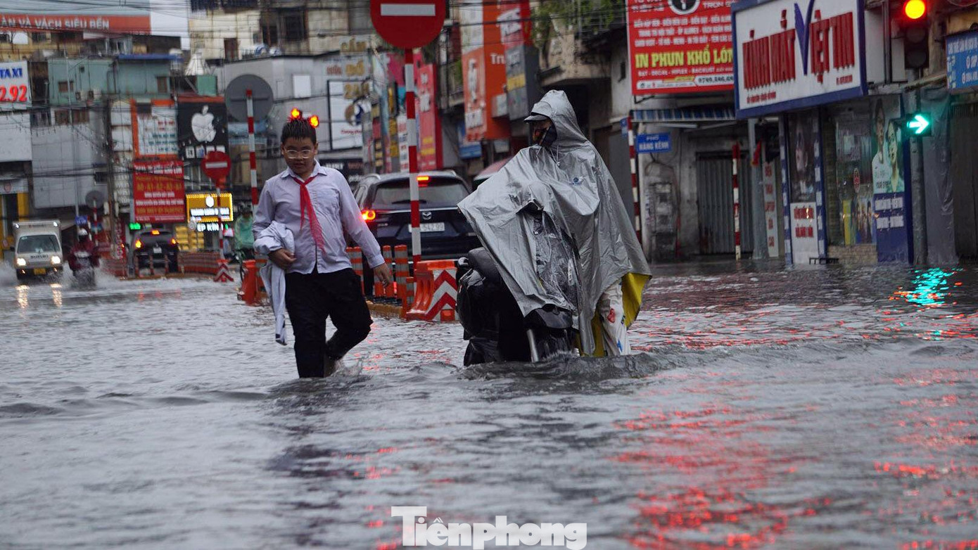 Xe chết máy, phụ huynh và học sinh lội nước qua phố ngập.