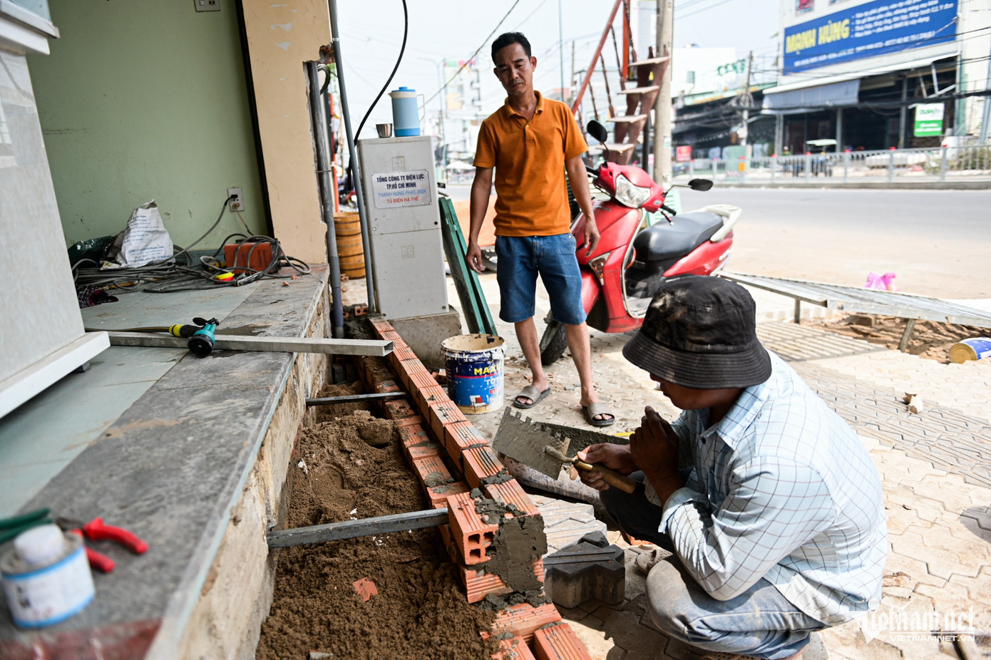Anh Tuấn (áo cam) cùng thợ đang sửa sang lại mặt tiền ngôi nhà. "Con đường được mở rộng ai cũng phấn khởi, nhưng việc các cột điện chưa di dời, công trình vẫn dở dang khiến khu vực xung quanh rất bụi", anh nói.