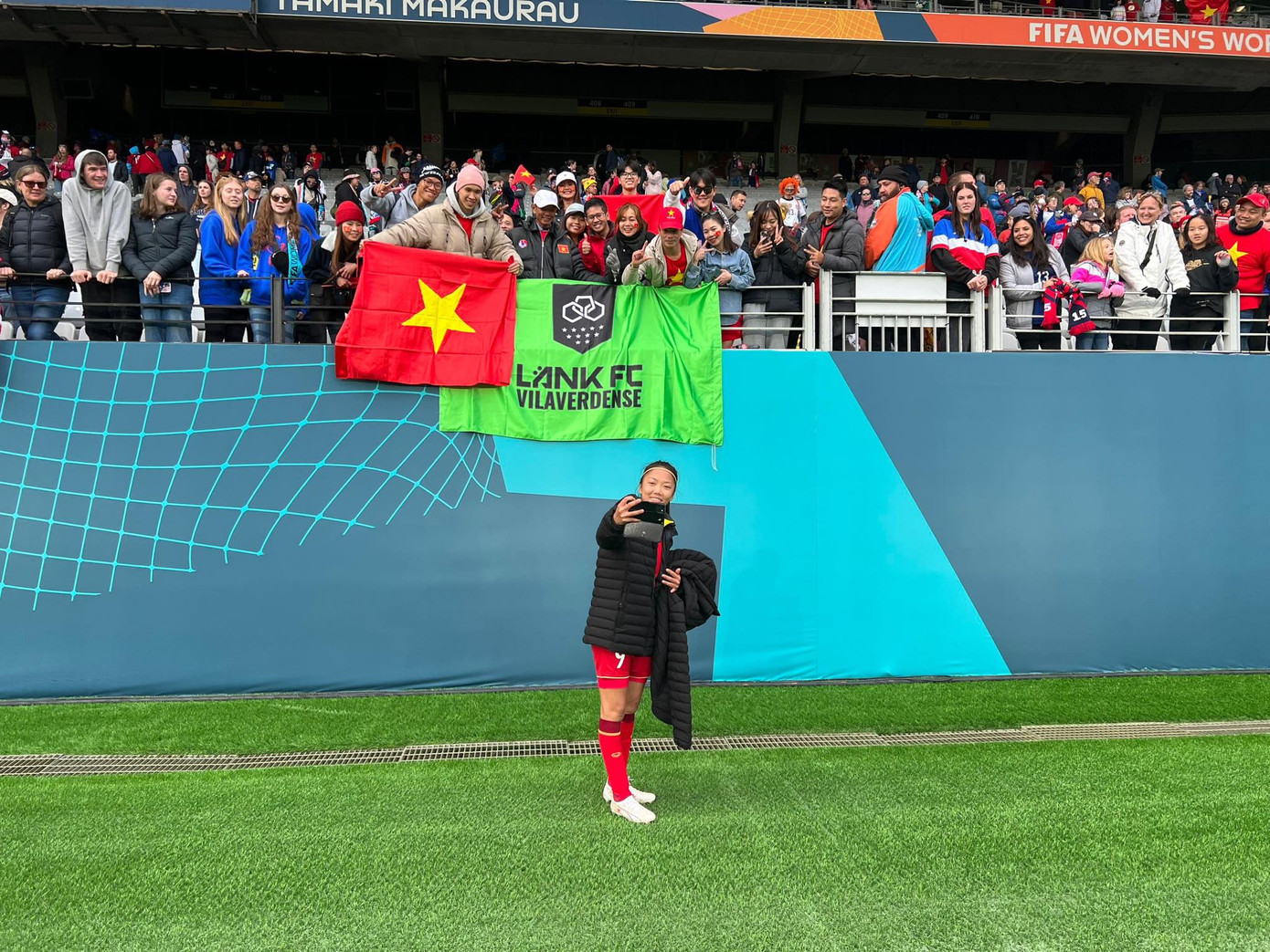 Huỳnh Như sung sướng selfie trước lá cờ Tổ quốc và Lank FC, đằng sau là ba má cùng CĐV Việt Nam, Bồ Đào Nha. (Ảnh: YouTuber Tuyền Văn Hóa)