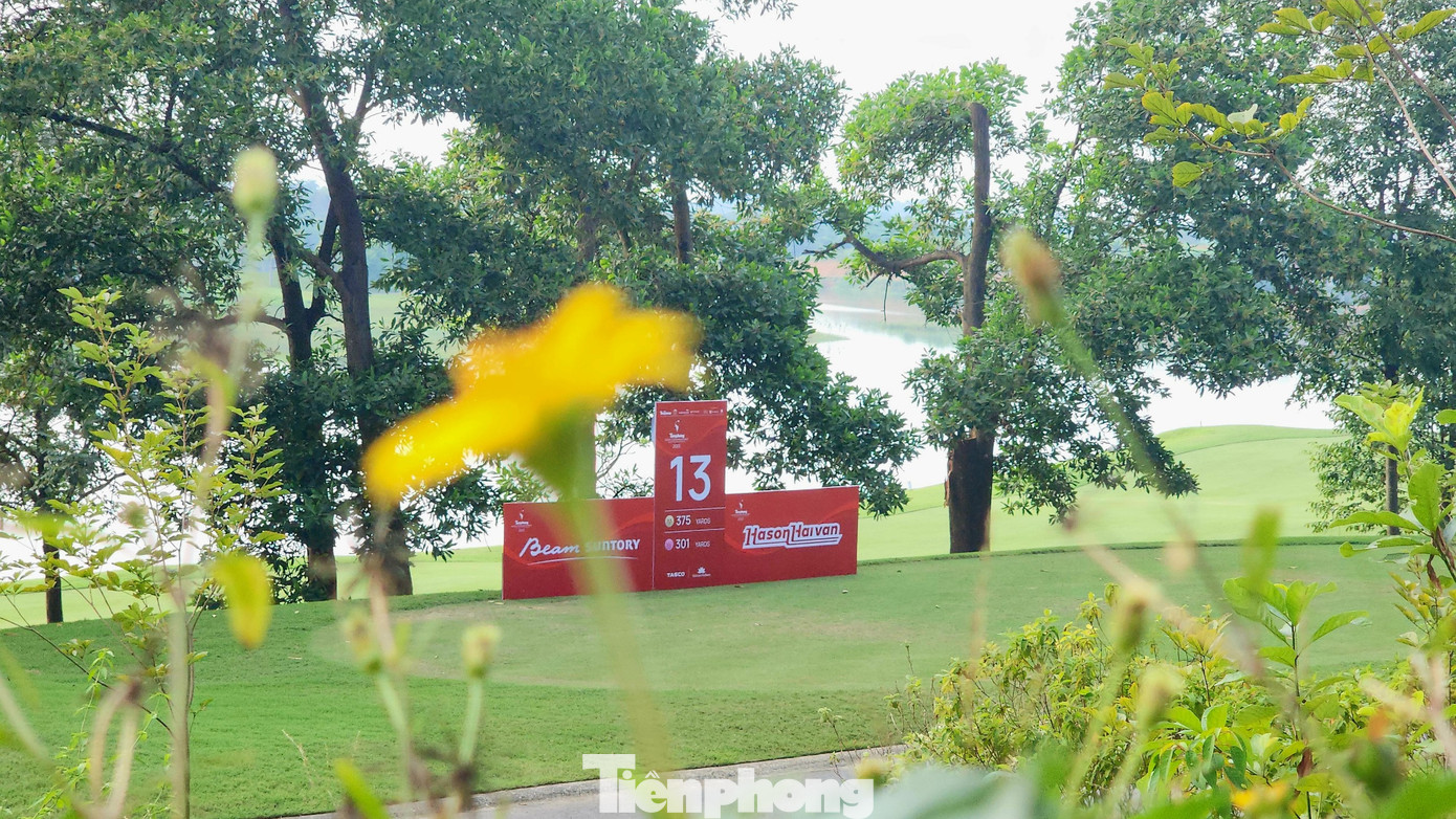 Mảng màu đỏ biểu trưng của Tiền Phong Golf Championship nổi bật giữa cỏ xanh, hoa vàng và hồ thu màu ngọc bích.