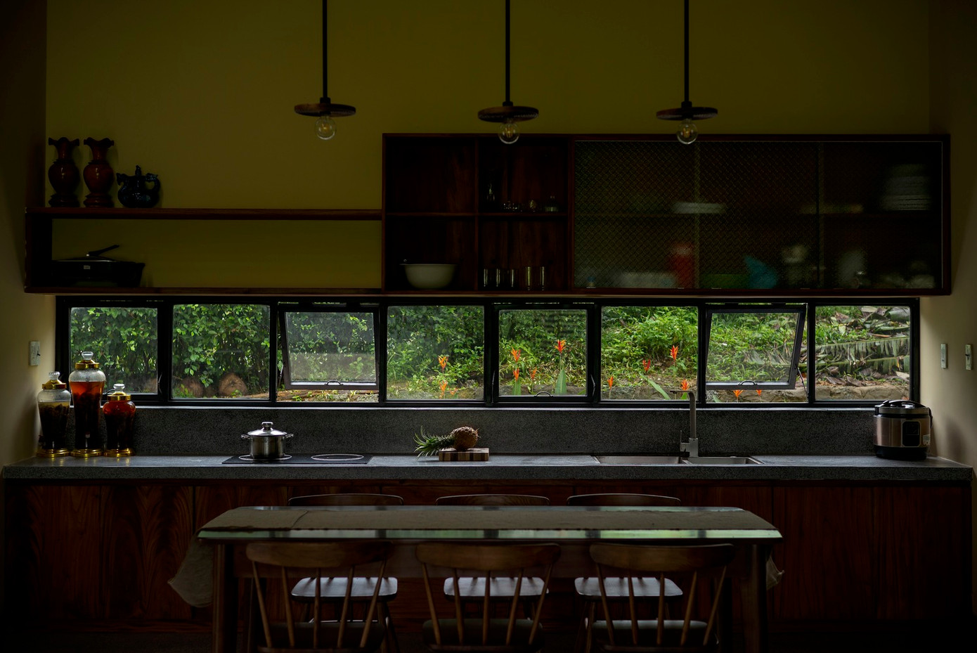 Các không gian chính tiếp cận trực tiếp với không gian ngoài trời thông qua các ô cửa và cửa sổ lớn, mang đến cảnh quan xanh tràn đầy sức sống và đón ánh sáng tự nhiên, cùng với khung cảnh nhìn ra cánh đồng lúa xanh và rừng cây tươi tốt.