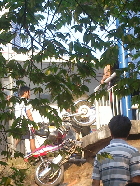 Chiếc xe máy bị xe tải hất văng xuống phía sau nhà chờ xe buýt