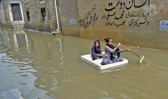 Hai bé gái Pakistan chèo bè tự tạo trên đường phố Karachi ngập lụt hôm 26/7. Ảnh: Arab News.