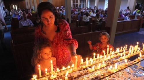 Một người phụ nữ và hai đứa con của cô thắp nến trên bàn thờ ông Mandela (Ảnh AP)