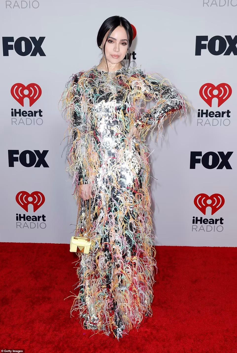 Ca sĩ Sofia Carson "kín cổng cao tường" với chiếc váy dài tay màu bạc đính sequin được trang trí bằng nhiều loại lông vũ sặc sỡ