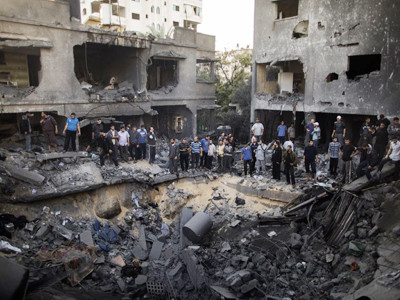 Người dân Palestine đứng quanh hố bom xuất hiện sau đợt không kích của Israel vào thành phố Gaza hôm 18-11