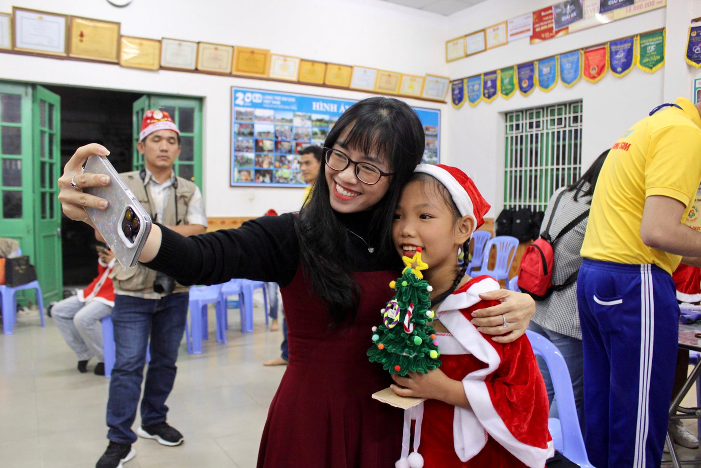 Được sự hướng dẫn tận tình của các tình nguyện viên, các bạn nhỏ nhanh chóng hoàn thiện sản phẩm và ghi lại kỷ niệm đáng nhớ. Chị Phạm Thị Thanh Trúc (cầm điện thoại) chia sẻ: “Hướng dẫn các em làm cây thông Noel không quá khó. Chỉ cần hỗ trợ các em sử dụng súng bắn keo để đảm bảo an toàn và cách làm cơ bản ban đầu, còn lại các em cứ tự do sáng tạo là sẽ ra được sản phẩm độc đáo theo sở thích”.