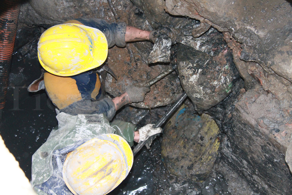 Xà beng được huy động để phá dỡ các bao tải bê tông ở miệng cống. Ảnh: Trường Phong