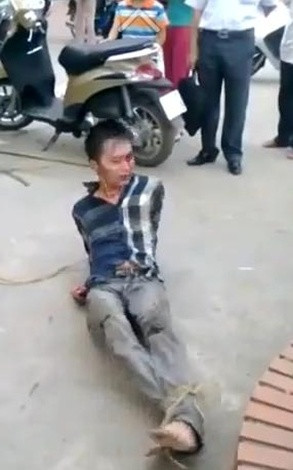 Nam thanh niên (cho là tên trộm) bị buộc chặt hay chân và hai tay, đang nằm lăn lộn trên mặt đất. (Ảnh cắt từ clip)