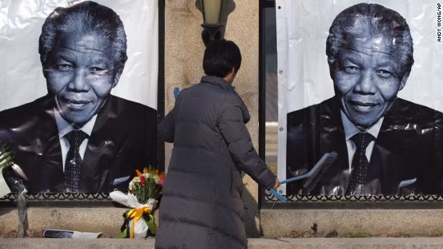 Một phụ nữ dọn dẹp bên ngoài đại sứ quán Nam Phi tại Bắc Kinh, chân dung ông Mandela được đặt tại đây, rất nhiều người cũng mang hoa tới viếng thăm.