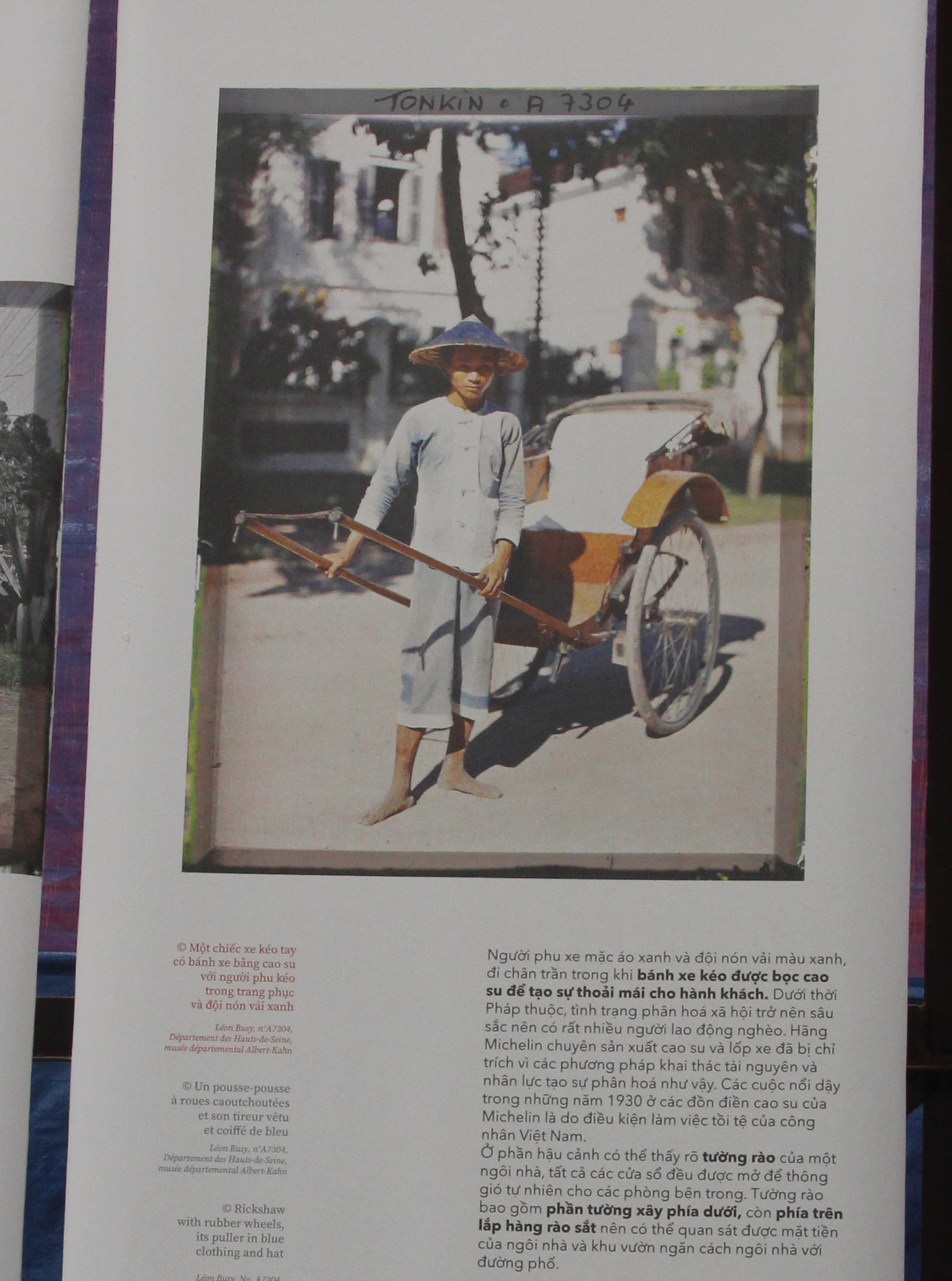 Một chiếc xe kéo tay có bánh xe bằng cao su với người phu kéo trong trang phục và đội nón vải xanh