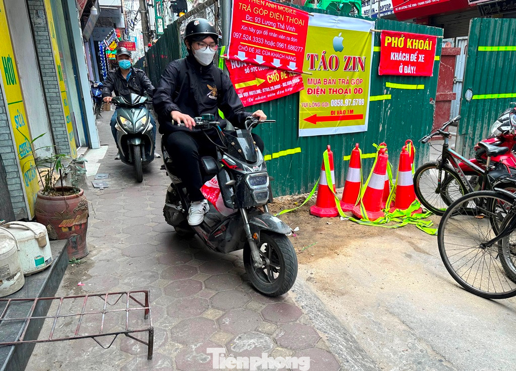 Người dân đi bộ và tham gia giao thông bằng xe máy luồn hàng rào công trường để đi lại.