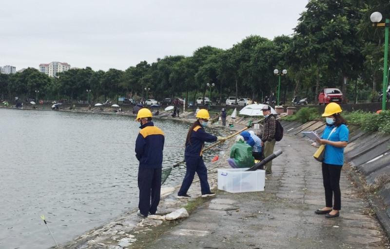 Nhân viên Cty Thoát nước thu gom rác trên hồ Định Công từ các tốp người câu cá xả ra. Bên cạnh là các tốp các ngồi câu cá có ô che mưa (màu trắng) vẫn diễn ra.