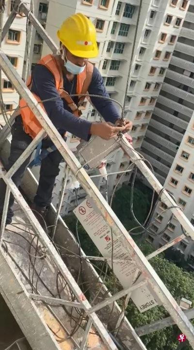 Một người thợ sơn cố buộc lại dây treo giá đỡ. Ảnh: Zaobao.