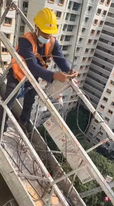 Một người thợ sơn cố buộc lại dây treo giá đỡ. Ảnh: Zaobao.