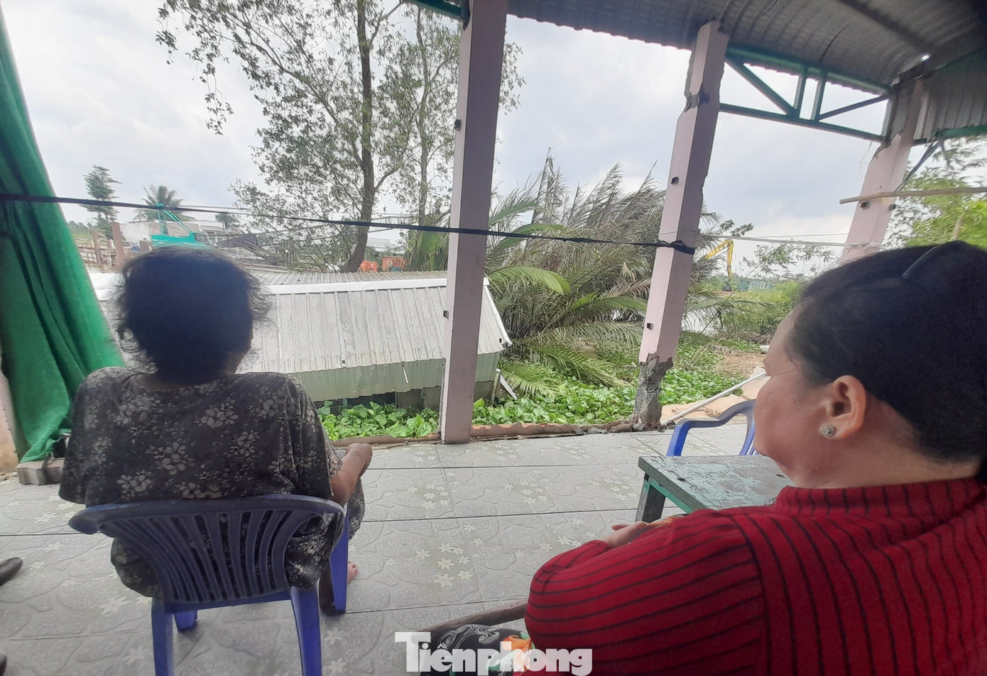 Mẹ con bà Võ Thị Xứng và chị Lê Thị Hồng Mai ngồi trước nhà mình, với hiện trường vụ sạt lở đến nay vẫn chưa được khắc phục. Ảnh: Cảnh Kỳ.