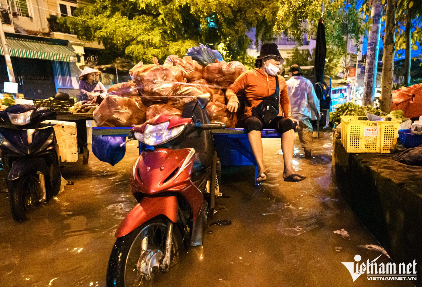 Người phụ nữ sau khi cùng chồng vận chuyển hàng rau củ quả đến chợ ngồi yên trên xe chờ nước rút mới có thể bày bán như bình thường.