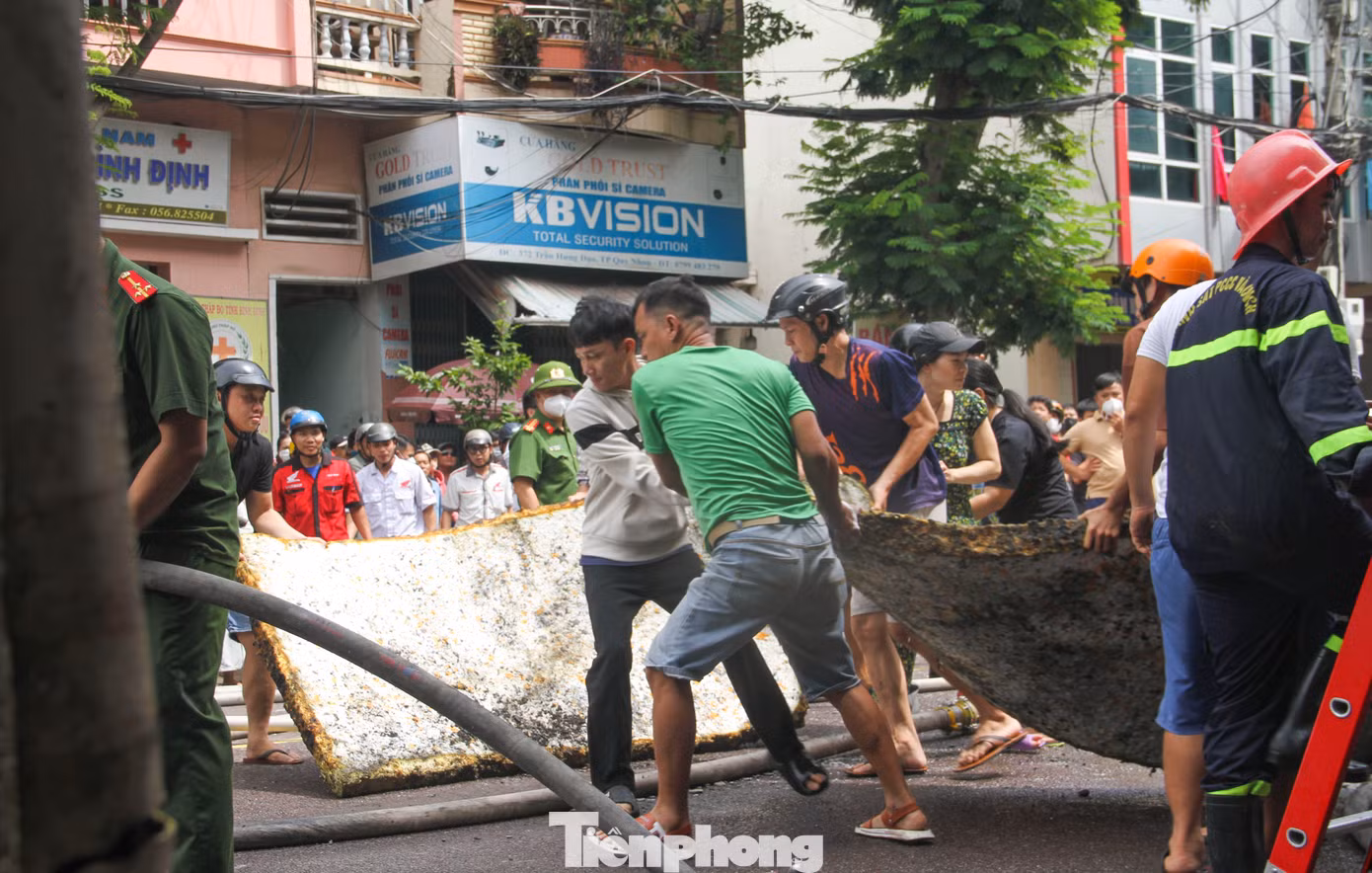 Người dân hỗ trợ di chuyển những tấm nệm bên trong căn nhà bị cháy ra ngoài. Ảnh: Trương Định