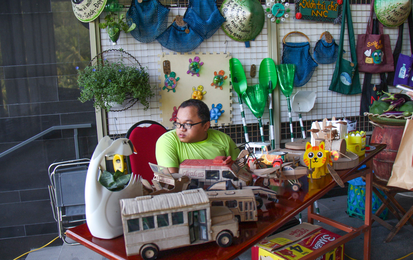 Gian hàng triển lãm đồ tái chế do các bạn khuyết tật ở Chi hội khuyết tật Nguyễn Nga thực hiện. Trong ảnh là anh Phan Huỳnh Anh Toan (35 tuổi, ở thị xã An Nhơn) bị tật 2 chân - một thành viên trong “mái nhà chung” của những người khuyết tật phụ trách công việc tái chế các vật dụng, đồ chơi từ rác thải.
