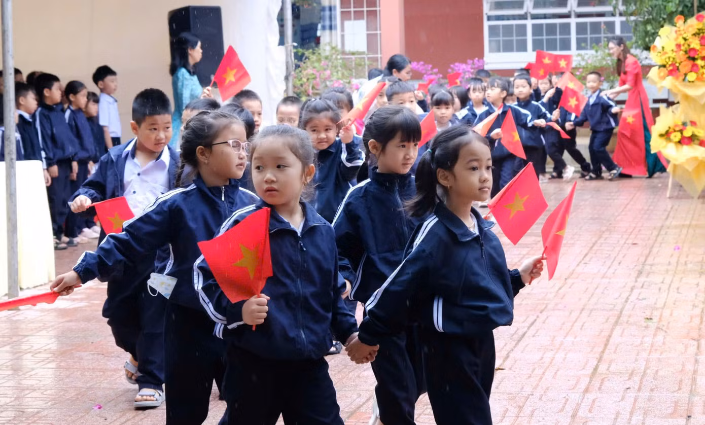 Các em học sinh phấn khởi cầm cờ diễu hành trong sân trường