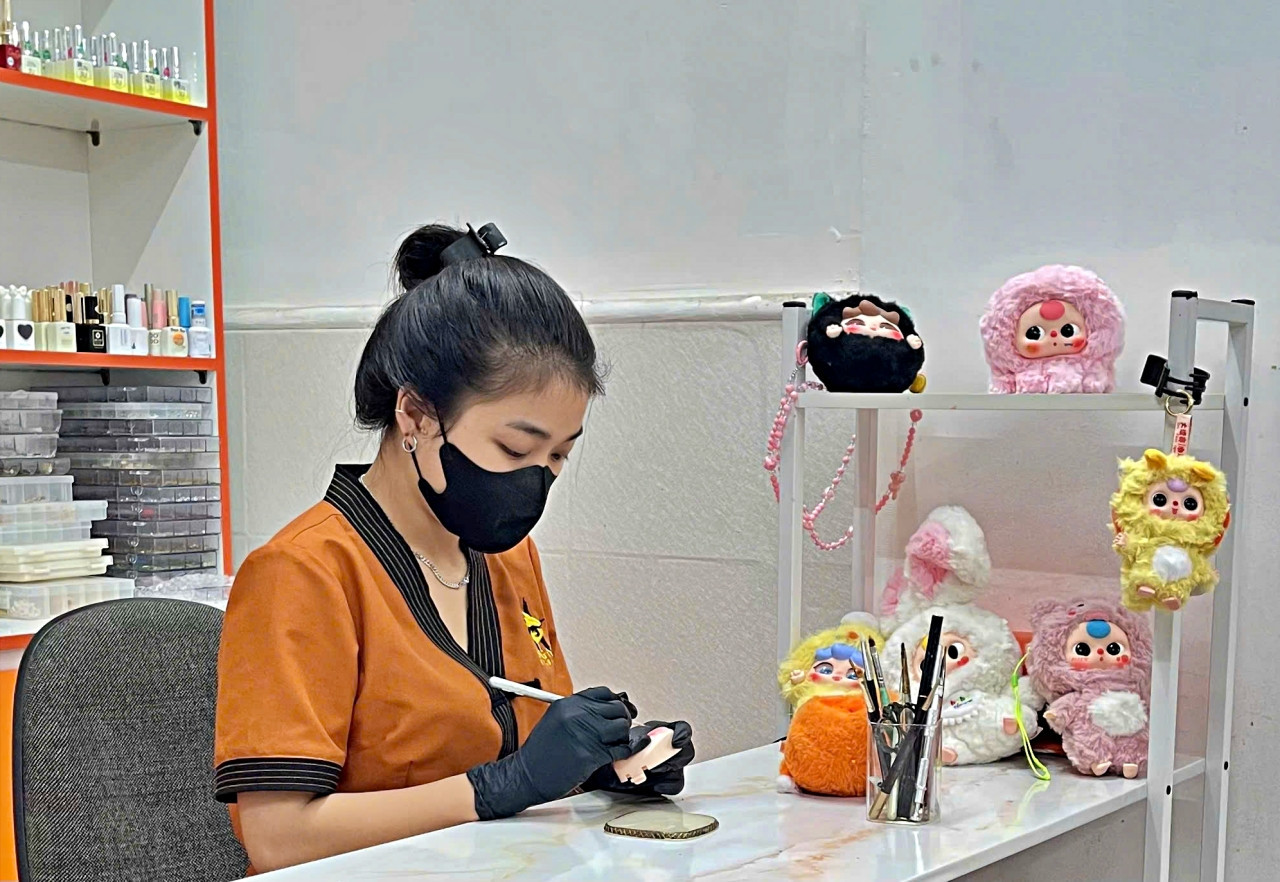 Ngọc Trúc tỉ mẩn vẽ lại mắt cho một con búp bê Baby Three tại tiệm nail mình đang làm việc. Ảnh: Ngọc Chi