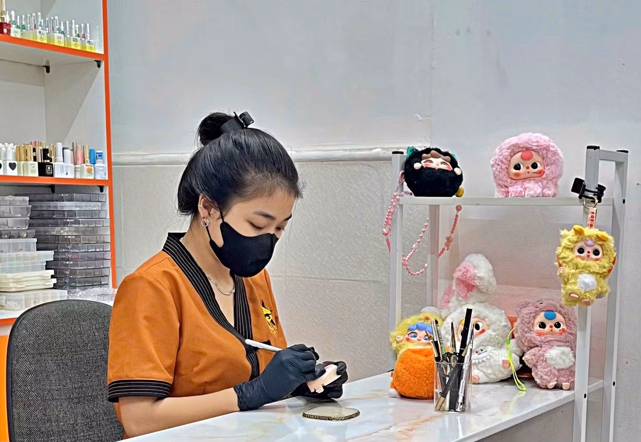 Ngọc Trúc tỉ mẩn vẽ lại mắt cho một con búp bê Baby Three tại tiệm nail mình đang làm việc. Ảnh: Ngọc Chi Ngọc Trúc tỉ mẩn vẽ lại mắt cho một con búp bê Baby Three tại tiệm nail mình đang làm việc. Ảnh: Ngọc Chi
