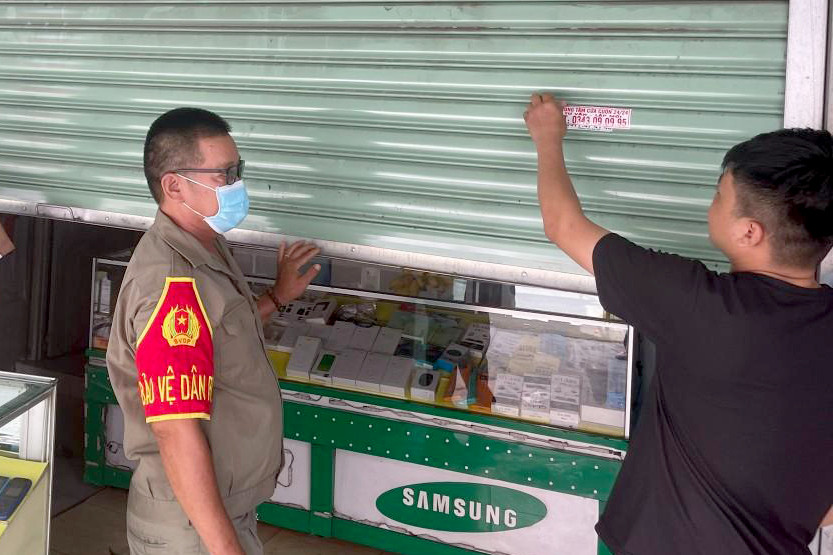 Lực lượng chức năng buộc nhóm T tự bóc gỡ các tờ quảng cáo dán trên cửa nhà dân (Ảnh: C.A.).