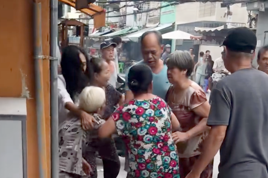 Cụ bà (người tóc bạc) bị chém và được người dân đưa vào bệnh viện cấp cứu. Ảnh cắt từ clip.