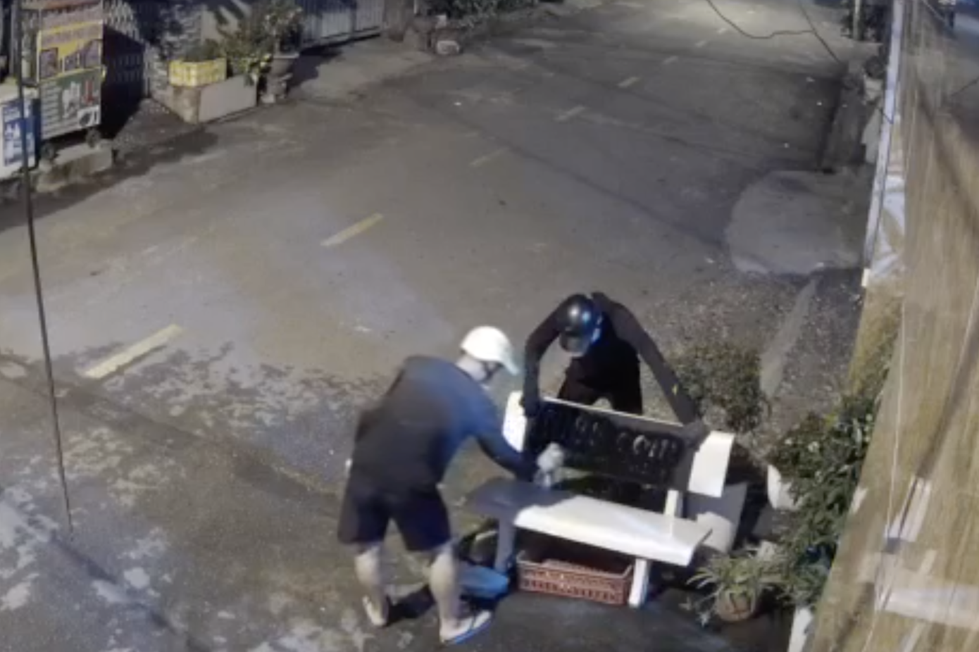 Hai thanh niên xịt sơn đen, in trang web cá độ lên ghế đá trước nhà dân (Ảnh cắt từ clip).