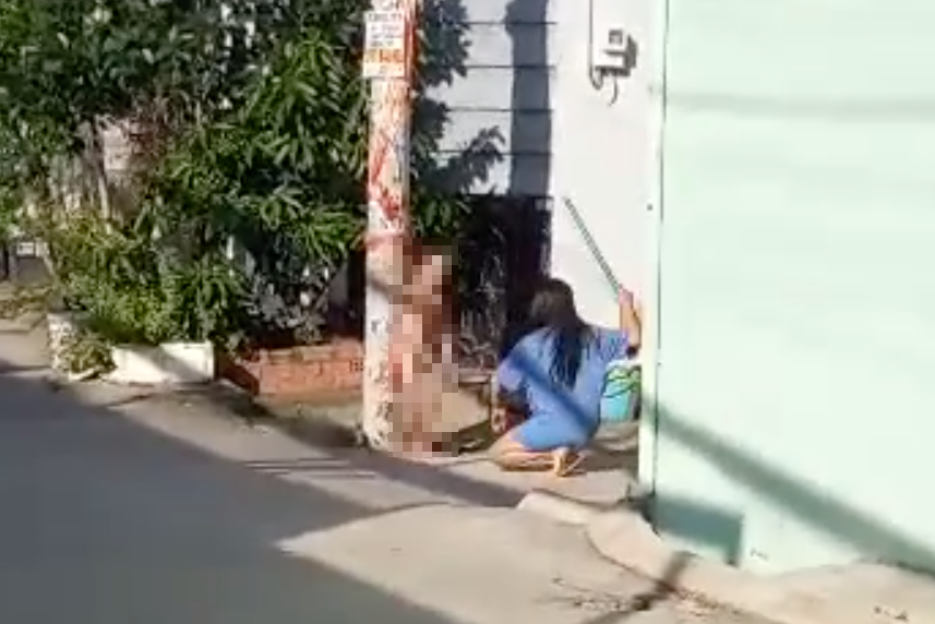 Bà T dùng chổi đánh bé trai không mặc quần áo và dựa vào cột điện. Ảnh cắt từ clip.