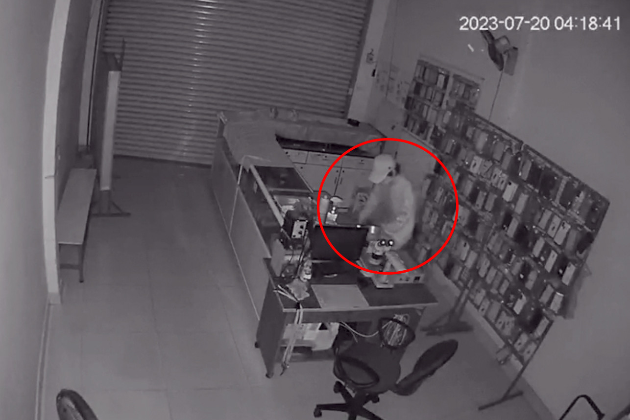 Người đàn ông lục lọi lấy tài sản trong cửa hàng điện thoại (Ảnh cắt từ clip).