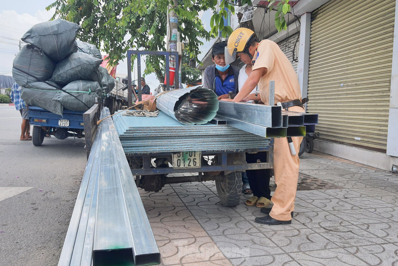 Lực lượng CSGT lập biên bản xử phạt tài xế điều khiển xe ba gác chở sắt thép có chiều dài vượt quá quy định. Ảnh: Hoàng Thuận.