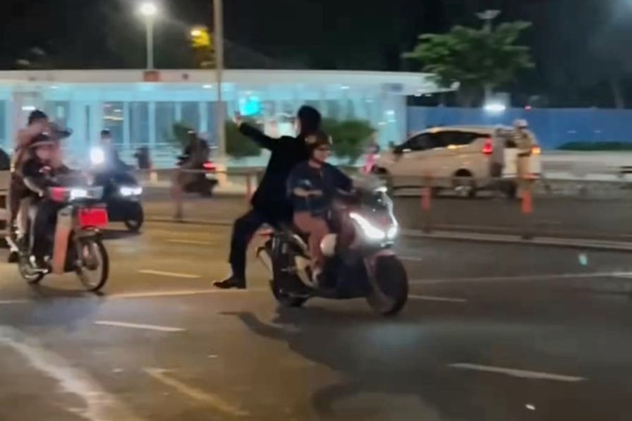 Hình ảnh T. lái xe chở nam thanh niên ngồi quay mặt về sau; L. chở một người khác đứng trên yên xe chụp hình. Ảnh cắt từ clip.