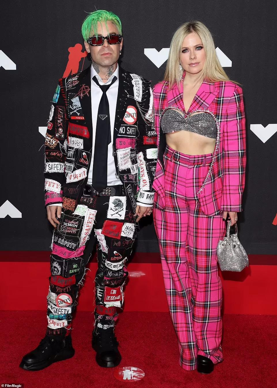 Avril Lavigne vẫn xứng đáng với danh xưng "công chúa nhạc pop-punk" ở tuổi U40 khi xuất hiện trong bộ đồ kẻ sọc màu hồng với áo ngực trễ nải. Tháp tùng cô là bạn trai Mod Sun trong bộ vest chắp vá.